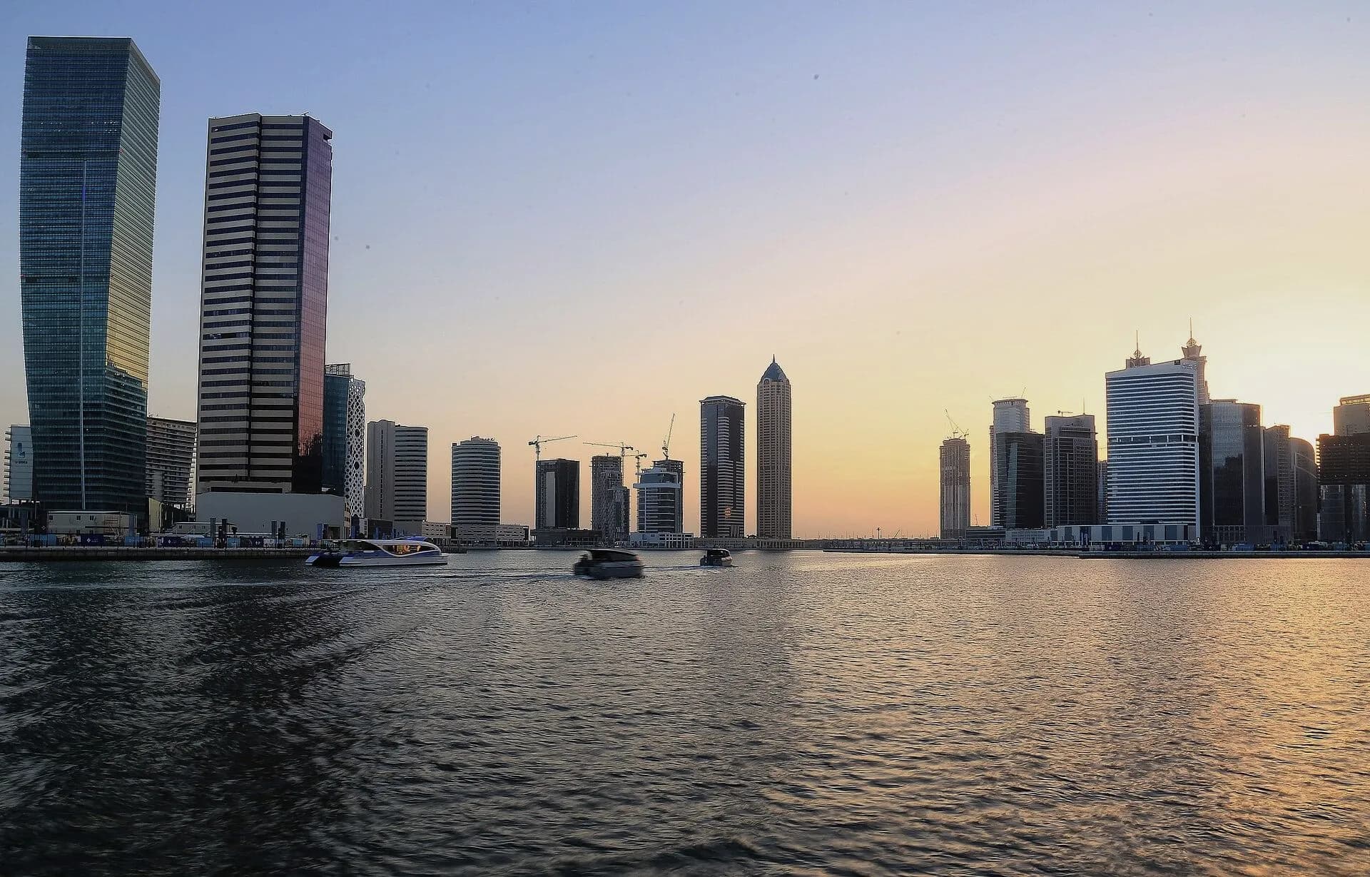 Business Bay towers along the Dubai Water Canal at sunset, framed in the MNV mark